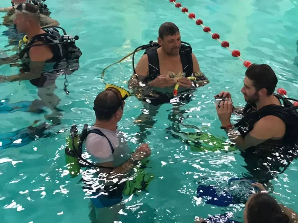 Instructeur geeft uitleg aan cursisten in het zwembad
